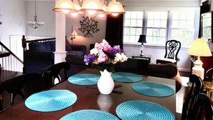 A dining area with a wooden table, blue placemats, a white vase with flowers, and a chandelier. - Ocean view 5-bedroom house in Narragansett with AC, WiFi, beach pass (Narragansett)