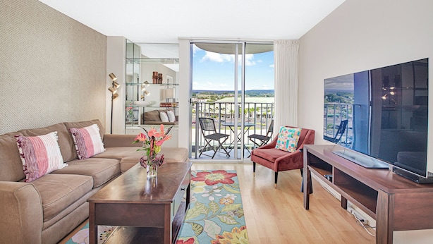 Un salon moderne avec un canapé, une table basse agrémentée d’un vase, un téléviseur et un balcon offrant une vue agréable.