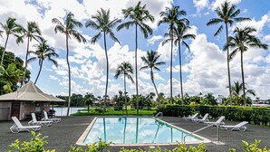 Ein Pool mit Liegestühlen, umgeben von Palmen und einem kleinen Gebäude.