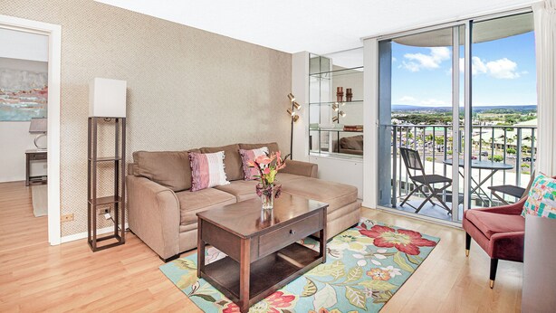 Ein modernes Wohnzimmer mit Sofa, Couchtisch und Blick auf eine Stadtlandschaft durch große Schiebegläser.