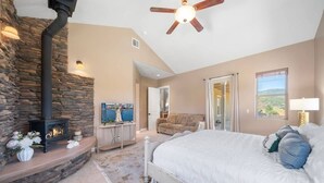 Ein Schlafzimmer mit Kamin aus Stein, einem Bett, einem Deckenventilator und Blick ins Freie.