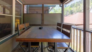 A wooden dining table with six chairs, a lamp, and a view of a red-roofed building through large windows. - Uptown Getaway - Lovely Condo in Downtown Tuscany Villas (Helen)