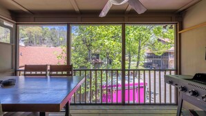 A balcony with a table and chairs, a grill, and a view of a pink dumpster and trees. - Uptown Getaway - Lovely Condo in Downtown Tuscany Villas (Helen)