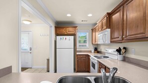 A kitchen with wooden cabinets, a white refrigerator, a stove, and a double sink. - Uptown Getaway - Lovely Condo in Downtown Tuscany Villas (Helen)