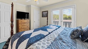 A bedroom with a large bed, a ceiling fan, a dresser, a television, and a door leading to a balcony. - Uptown Getaway - Lovely Condo in Downtown Tuscany Villas (Helen)