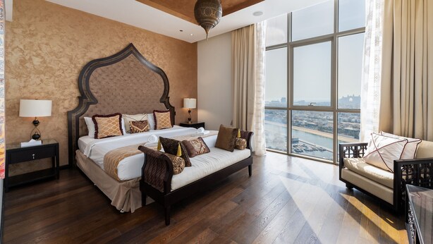 A spacious bedroom with a large bed, a sofa, and a view of a cityscape through large windows. - 4BR Maid Palm Penthouse w Atlantis Views Beach Access (Dubai)