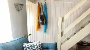 Un canapé bleu orné d’un coussin à motifs géométriques, un mur blanc avec un luminaire suspendu et un escalier avec une rampe blanche.