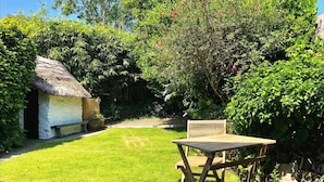 Une cabane à toit de chaume, une table en bois et un banc dans un jardin luxuriant.