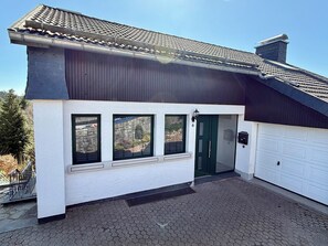 Una casa a due piani con facciata bianca, tetto marrone scuro e un garage.