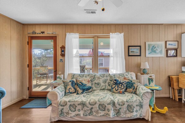 A cozy room with a wooden paneled wall, a patterned sofa, a dining table, and a view through a glass door.