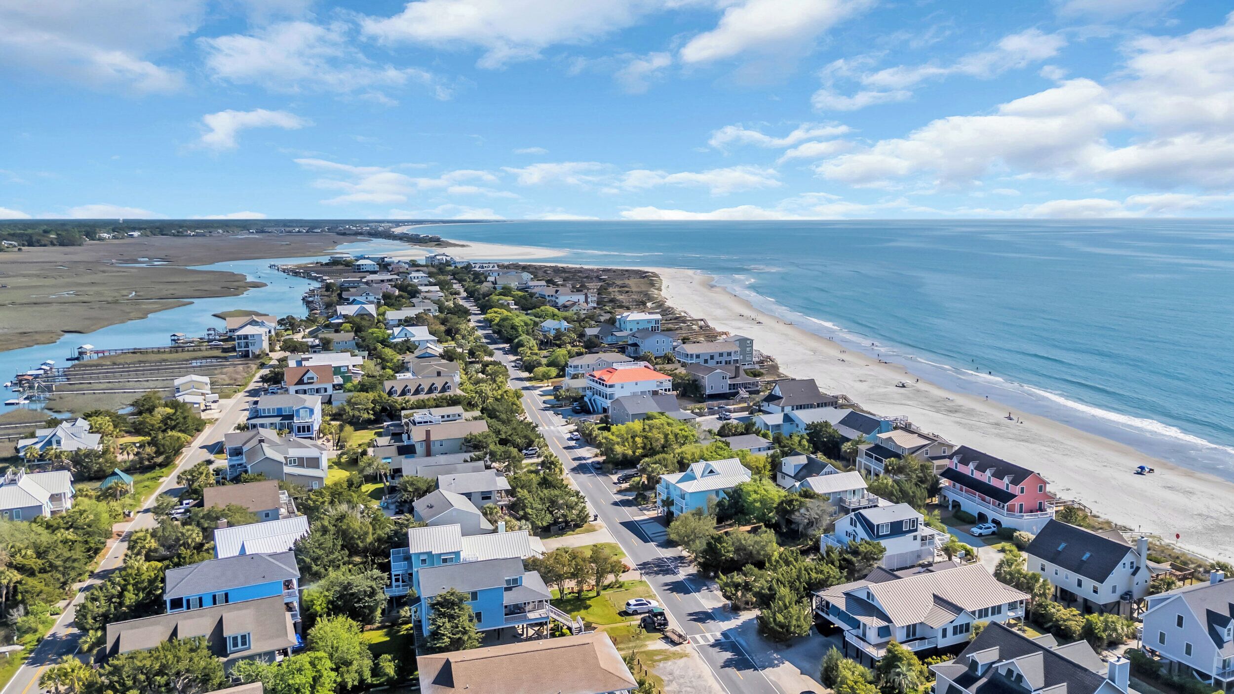 An aerial view of a coastal residential area with houses, a beach, and a marina.