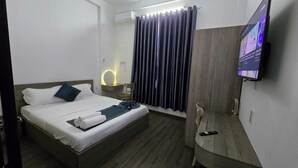 Una camera d'albergo con un letto, una scrivania, una sedia, una televisione e una tenda.
