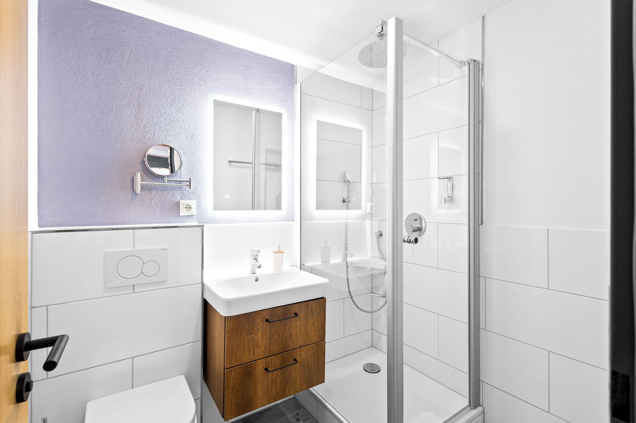 Une salle de bain moderne avec une douche à l’italienne en verre, un lavabo blanc et un meuble-lavabo en bois.
