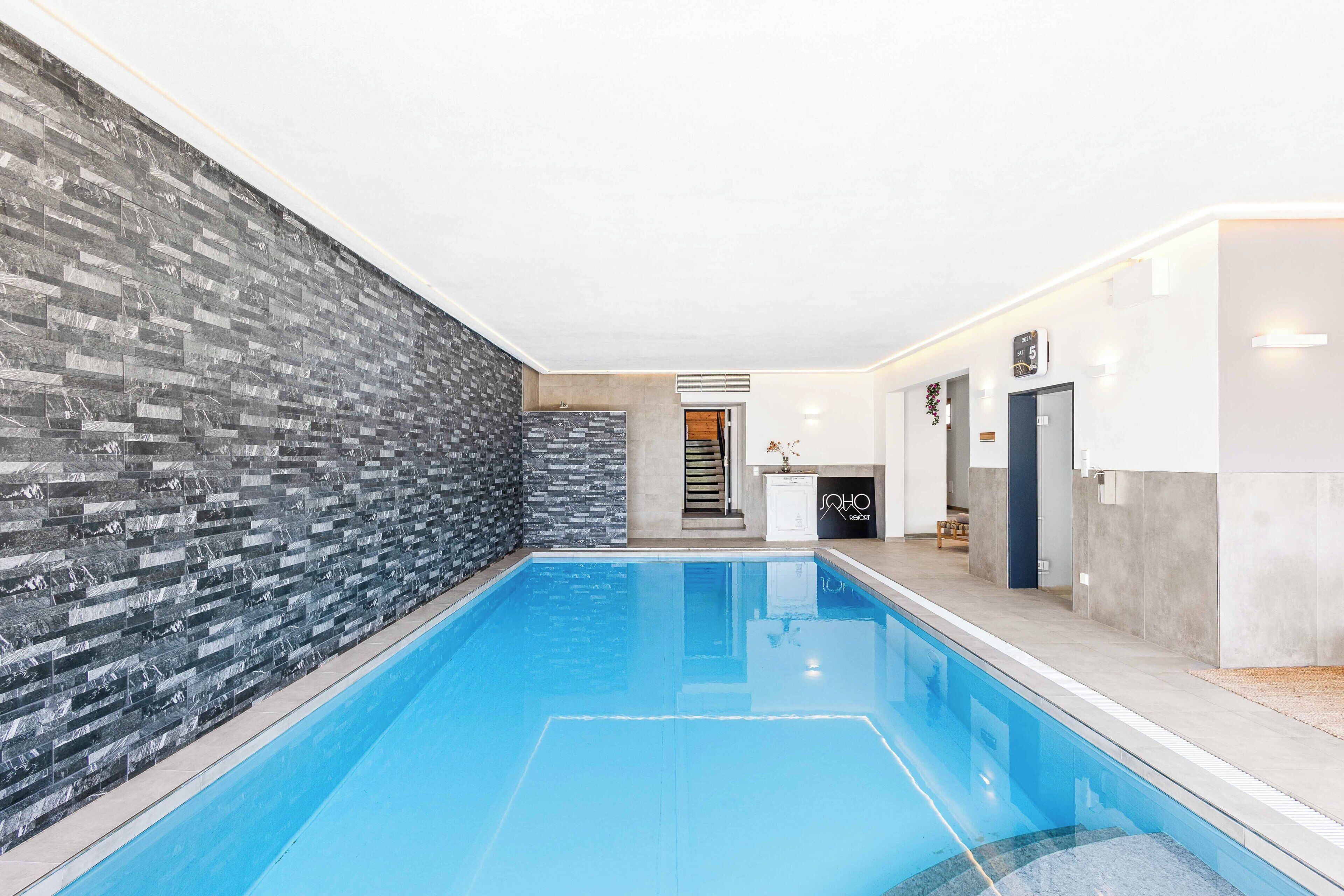 A modern indoor swimming pool with a stone wall on one side and a clean, tiled floor.