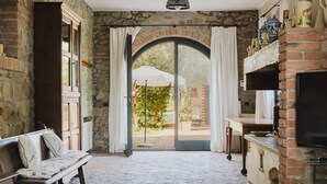 A room with a stone wall, a bench with cushions, a fireplace, and a large window with curtains. - Villa San Girolamo (Toscana)