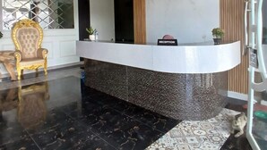 A reception area with a marble reception desk, a gold chair, and a potted plant. - RPCC D'Homestay (Rantauprapat)