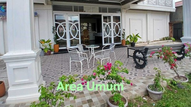 A covered outdoor seating area with tables and chairs, surrounded by potted plants and flowers. - RPCC D'Homestay (Rantauprapat)