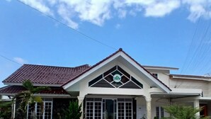 A house with a red-tiled roof, a central entrance with a geometric design, and a satellite dish on the roof. - RPCC D'Homestay (Rantauprapat)
