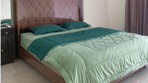 A bed with a tufted headboard, a green quilted bedspread, and two teal pillows. - RPCC D'Homestay (Rantauprapat)