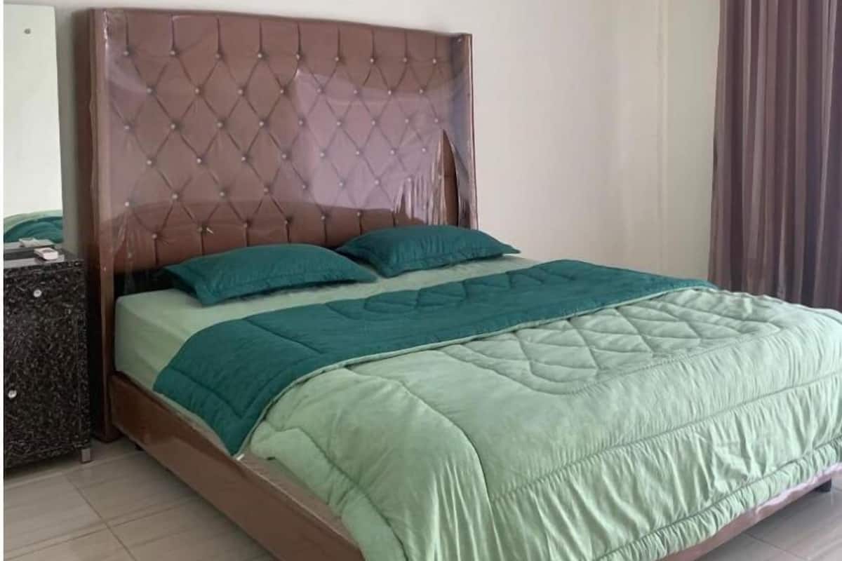 A bed with a tufted headboard, a green quilted bedspread, and two teal pillows.