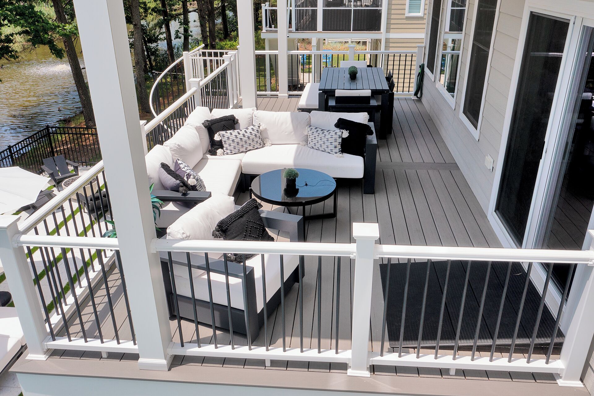 A covered outdoor seating area with a white railing, a sofa, a table, and a view of a body of water.