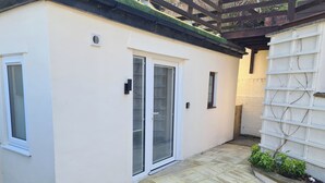 A small, single-story building with a white exterior, a door with a glass panel, and a small window. - Conwy Charm Cottage - 3 Bedroom Retreat Sleeps 7 (Penmaenmawr)