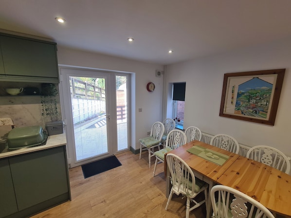 A dining area with a wooden table and white chairs, a kitchen with a green countertop, and a door leading outside.