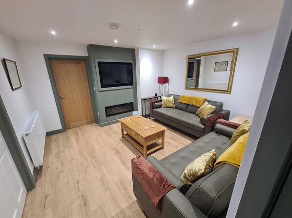 A living room with a sofa, coffee table, TV, fireplace, and a mirror on the wall. - Conwy Charm Cottage - 3 Bedroom Retreat Sleeps 7 (Penmaenmawr)