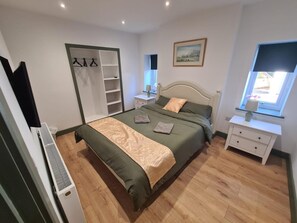 Un dormitorio con cama, armario, mesita de noche, ventana y un cuadro en la pared.
