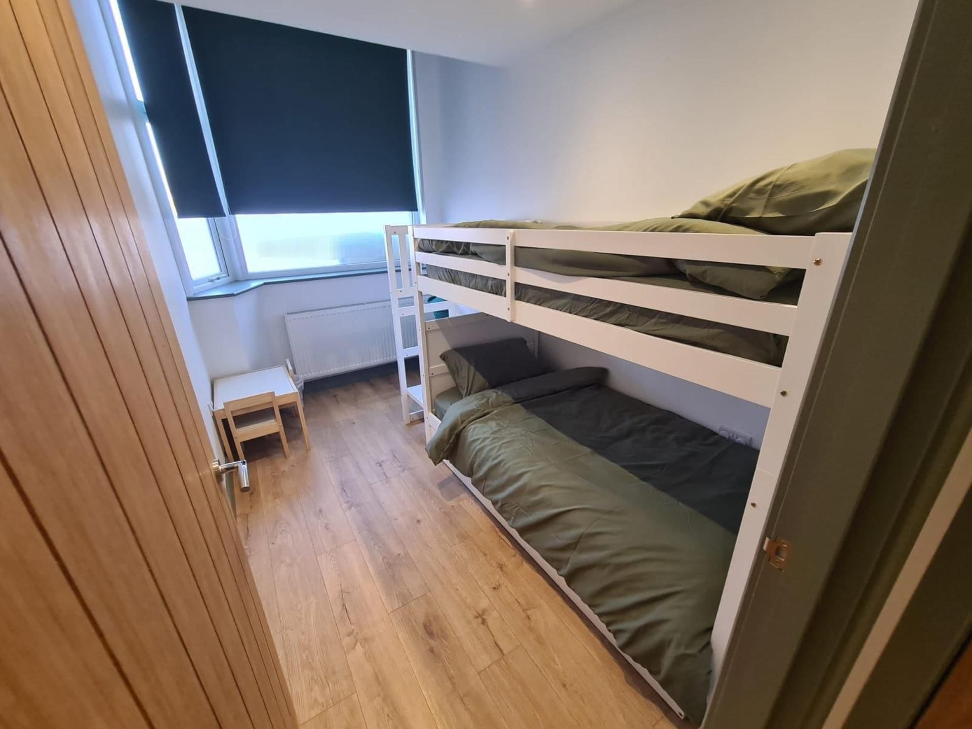 Quarto compacto com uma cama beliche, um banquinho de madeira e uma janela que oferece luz natural.