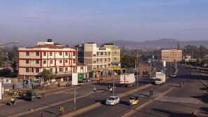 A wide street with buildings on either side, a clear sky, and distant mountains.