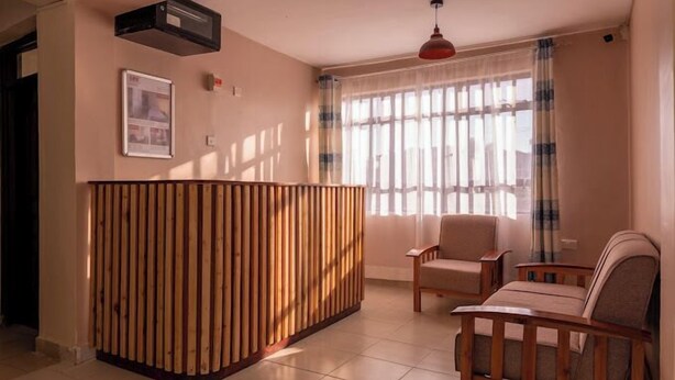 A living room with a wooden reception desk, two armchairs, a red pendant light, and a window with curtains.