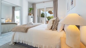 Ein modernes Schlafzimmer mit einem großen Bett, einer Nachttischlampe, einem Spiegel und Blick ins Freie.