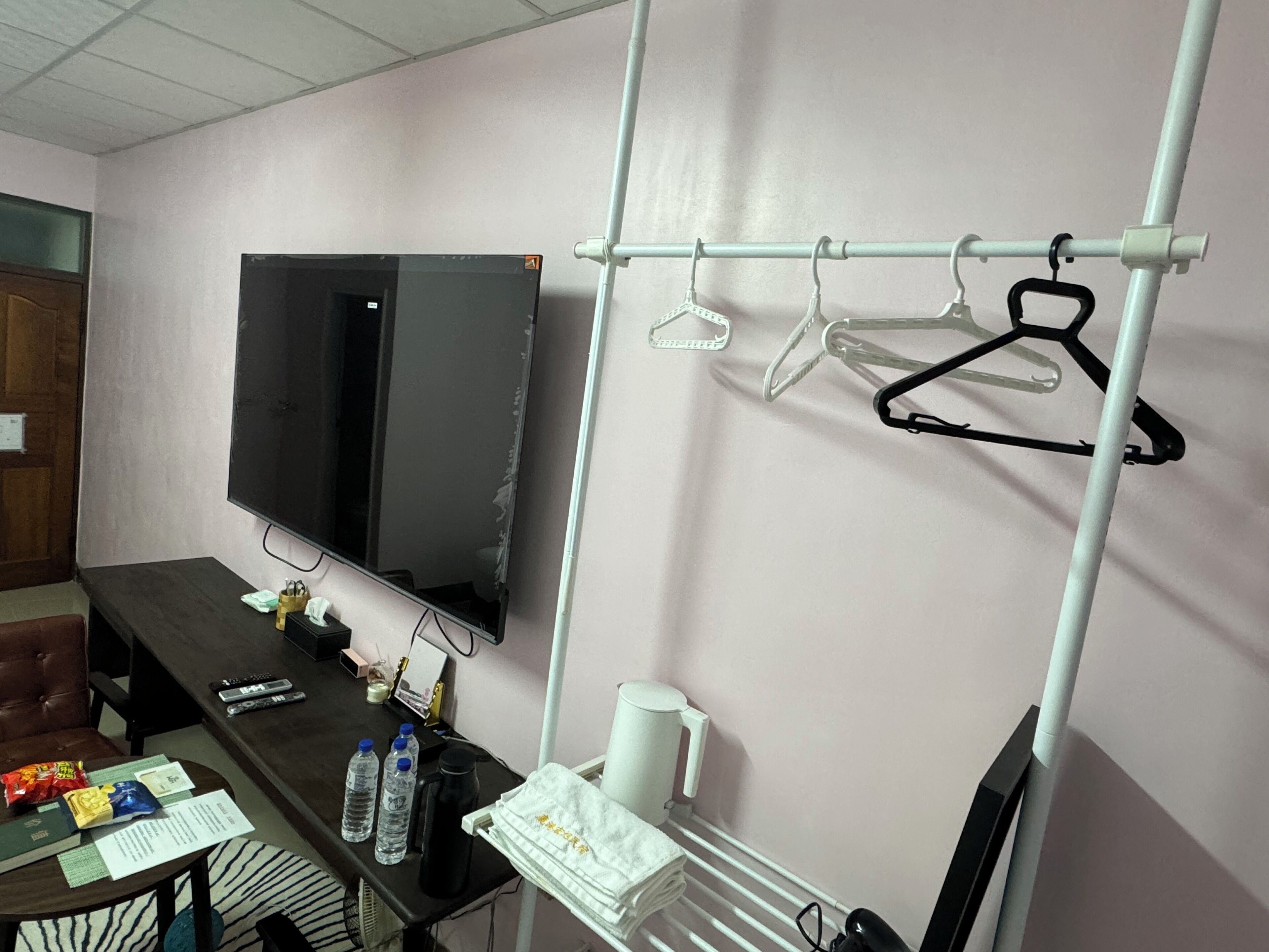 A room with a TV mounted on the wall, a desk with a chair, a coat rack, and a radiator.