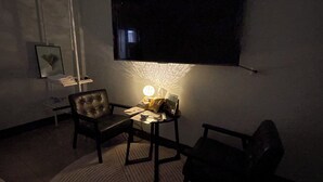 A dimly lit room with a large flat-screen TV mounted on the wall, a small table with a lamp, and two leather chairs. - Lukang Hung-shiu Homestay (Lukang)