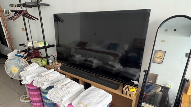 A room with a large flat-screen TV, a fan, and several rolled-up towels on stools. - Lukang Hung-shiu Homestay (Lukang)
