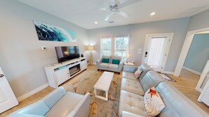 A modern living room with a flat-screen TV, a sofa set, a coffee table, and a ceiling fan.
