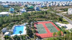 An aerial view of a coastal residential area with houses, a tennis court, and a swimming pool.