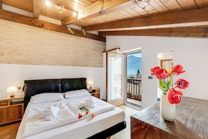 A hotel room with a bed, a nightstand, a lamp, a vase with flowers, and a balcony with a view. - Casa Del Profeta (Arco)