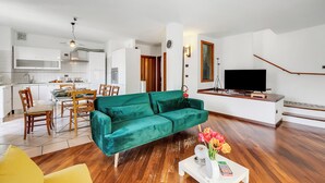 A modern living room with a green sofa, wooden dining table, and a TV on a stand.