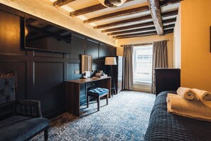 A hotel room with a dark wooden desk, a chair, a bed with a rolled-up towel, a lamp, and a window with curtains. - Richard III Hotel (Middleham)