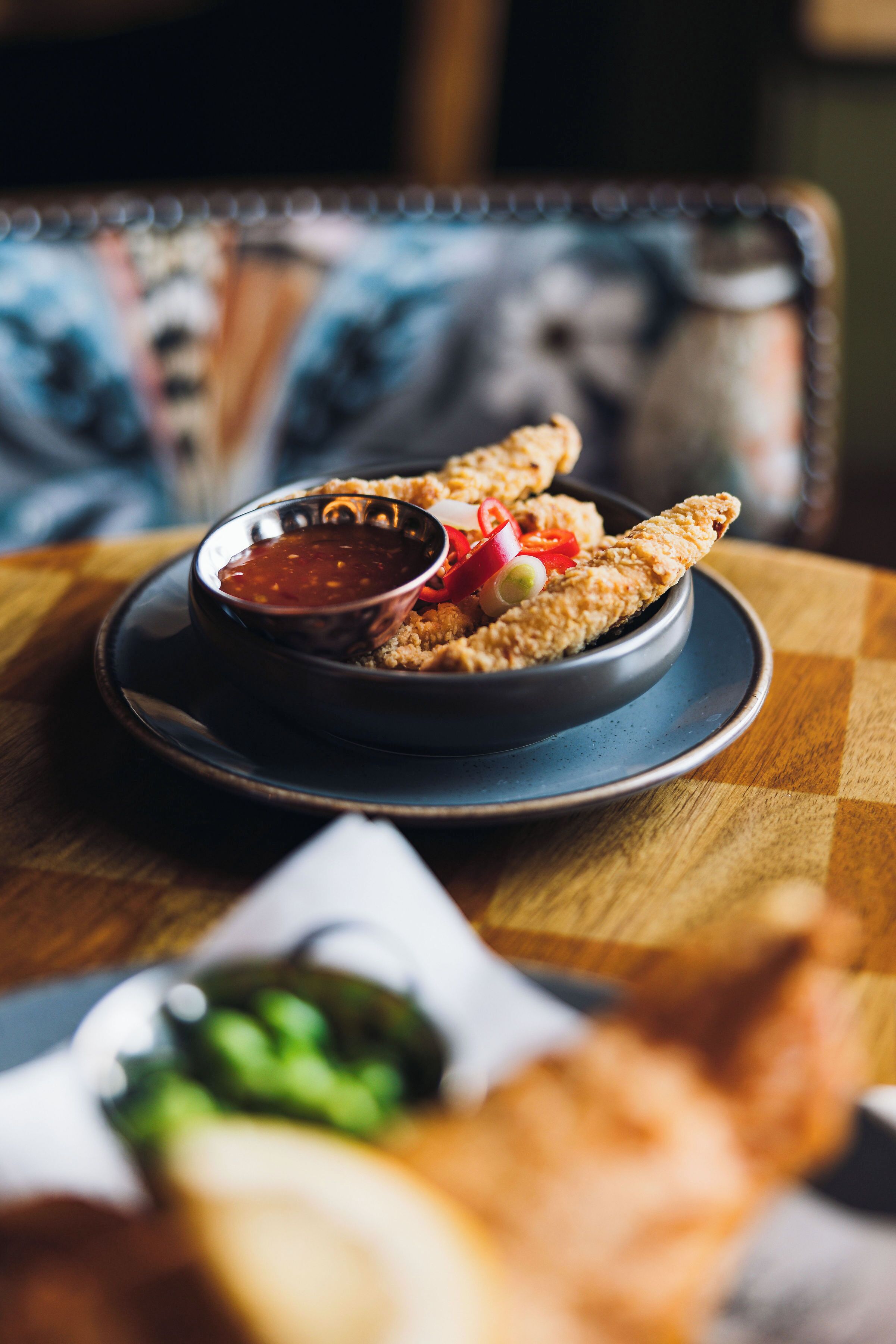 Une assiette de fritures, accompagnée d’une sauce pour tremper et de légumes, est posée sur une table.