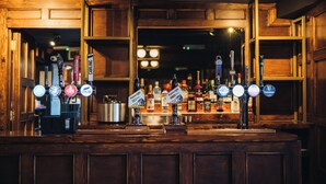 Un bar con múltiples grifos de cerveza y una variedad de botellas al fondo.