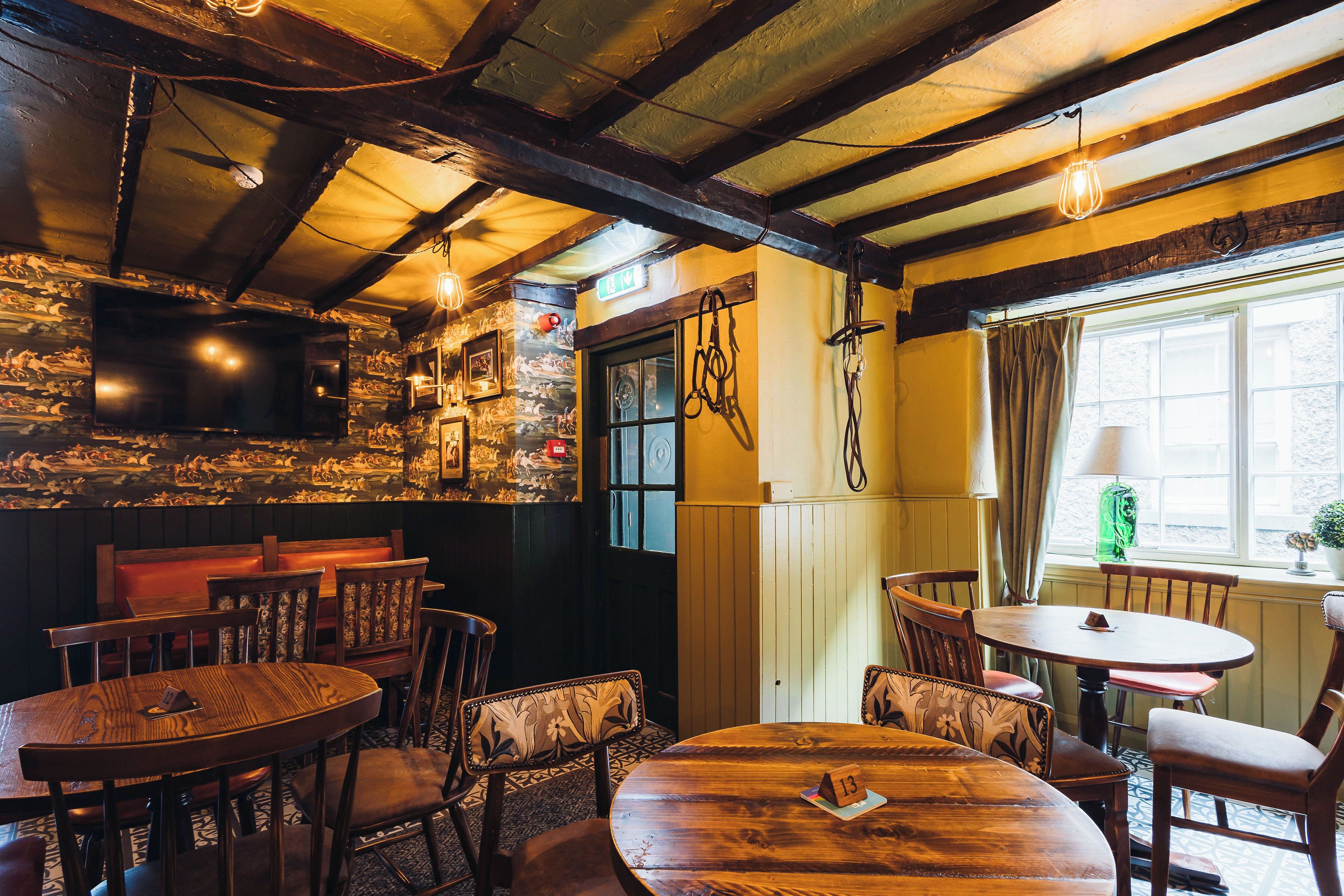 L’intérieur d’un pub à l’ambiance rustique, avec des meubles en bois, un téléviseur fixé au mur et une fenêtre ornée de rideaux.