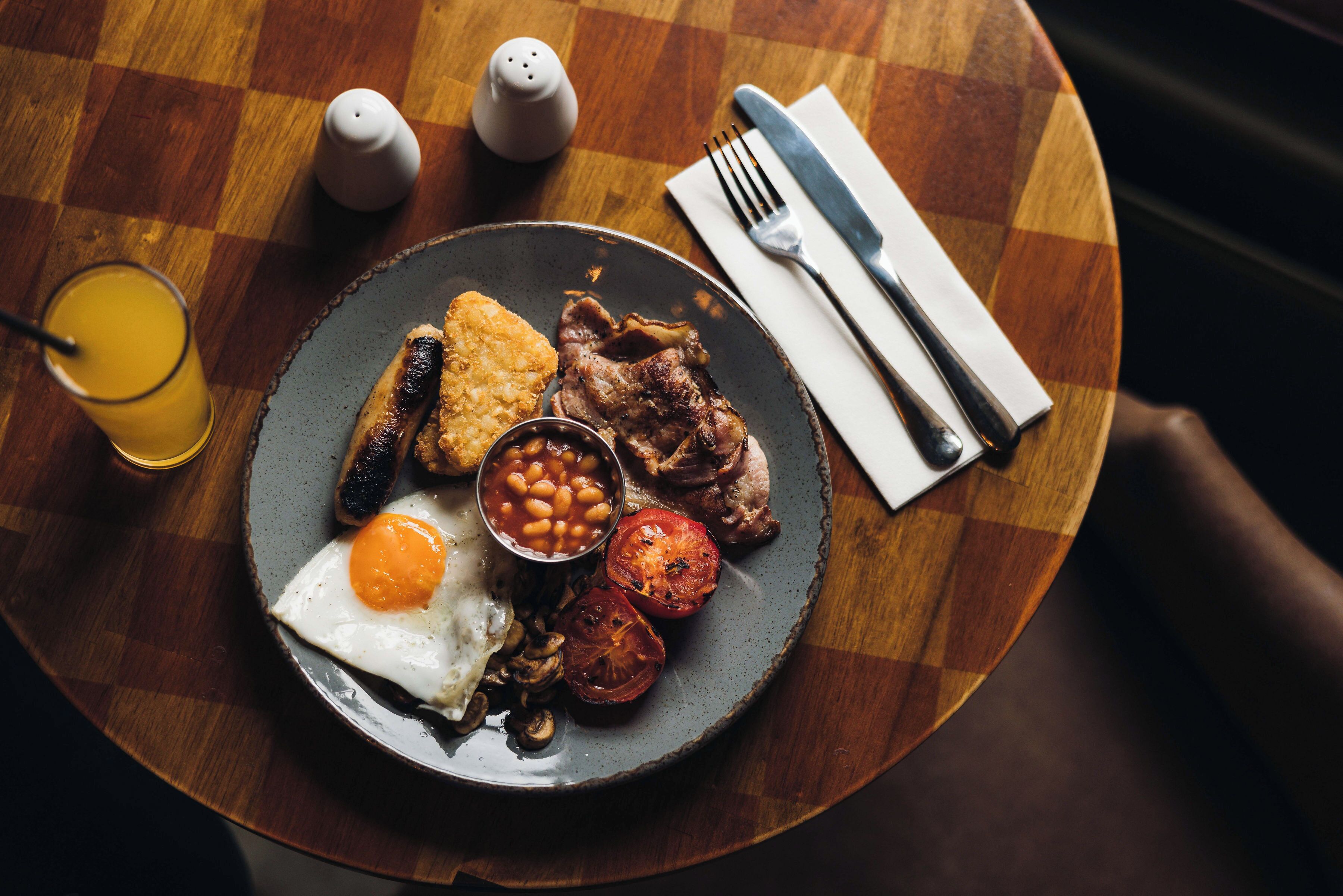 A breakfast plate with eggs, beans, tomatoes, and meat on a checkered tablecloth.