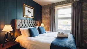Una cama bien hecha con cabecera capitonada, dos lámparas de noche y una ventana con cortinas.