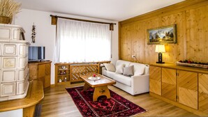 Een woonkamer met een witte bank, houten kasten, een televisie en een rood vloerkleed.