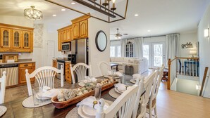 A spacious kitchen with wooden cabinets, a dining area with white chairs, a large wooden table set for a meal, and a staircase leading to a loft bedroom area.