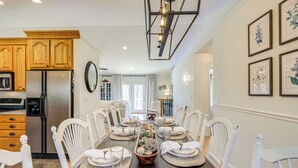 A dining room with a wooden table set for six, surrounded by white chairs.