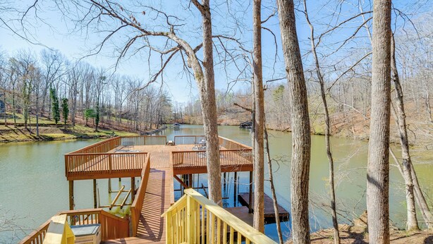 A wooden deck with a staircase leading to a platform over a body of water, surrounded by trees.